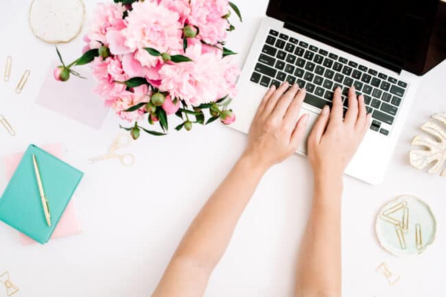 Womans hands on computer keyboard on desk with flowers.