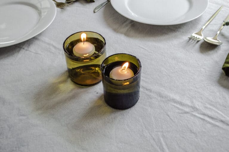 Wine bottle floating candle holders with lit candles on a dining table.