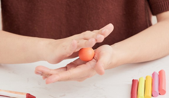 woman rolling orange clay ball between her hands.