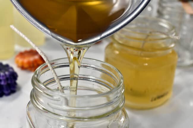 Melted candle wax being poured into a glass jar.