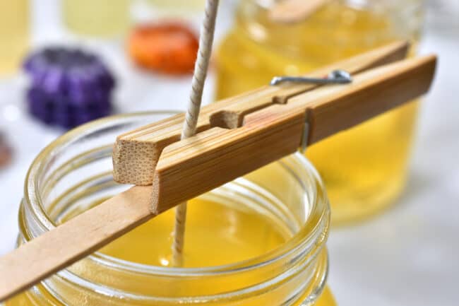 Wooden clothes peg securing a candle wick over a glass jar of melted candle wax.