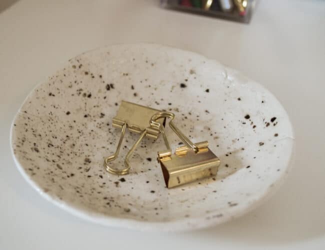 Cream & black speckled bowl on tabletop with 2 clips inside.