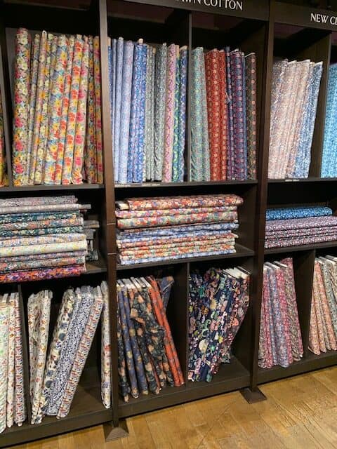 Selection of bright and colorful fabrics on wooden shelves inside Liberty's of London.