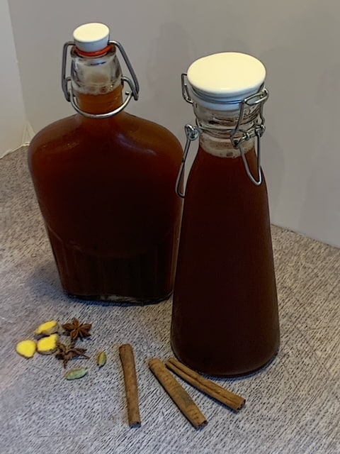 2 glass bottles Chai Tea concentrate sitting on a table with Cinnamon sticks around.