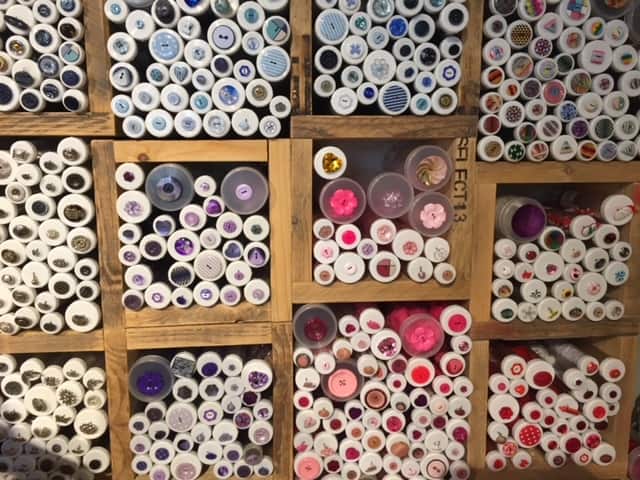 Display of various colored buttons in tubes in a wooden display rack inside Liberty's of London.