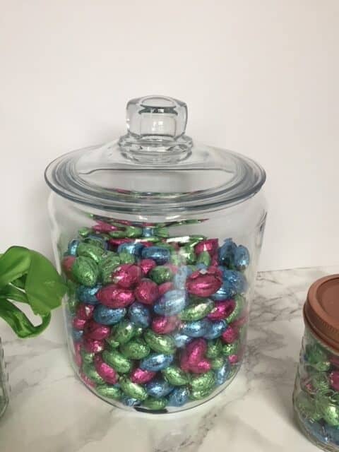 Glass storage jar filled with chocolate foil wrapped easter eggs.