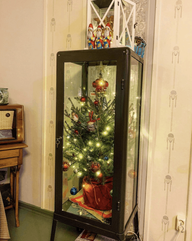 Christmas tree displayed inside a black glass door cabinet.