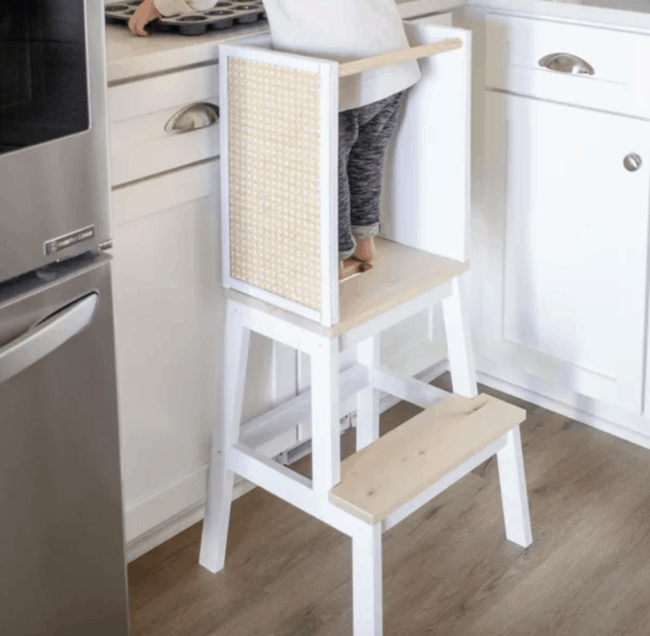 Child standing on white and cane learning tower.