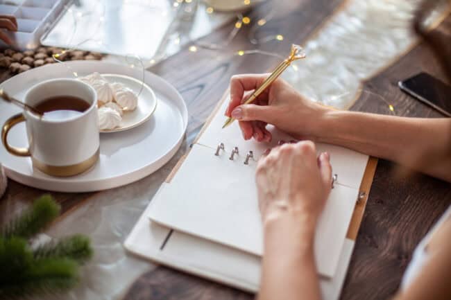 Woman writing in a paper planner, with a cup of tea nearby