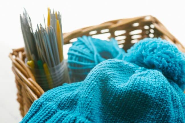 Blue knitting with blue yarn and knitting needles in a basket.