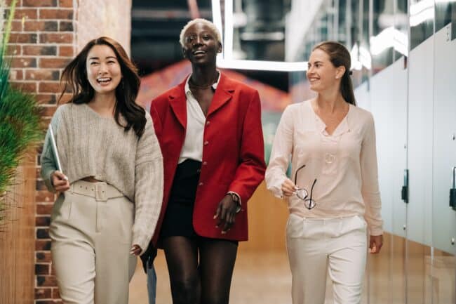 3 women dressed in business attire walking down a hallway.